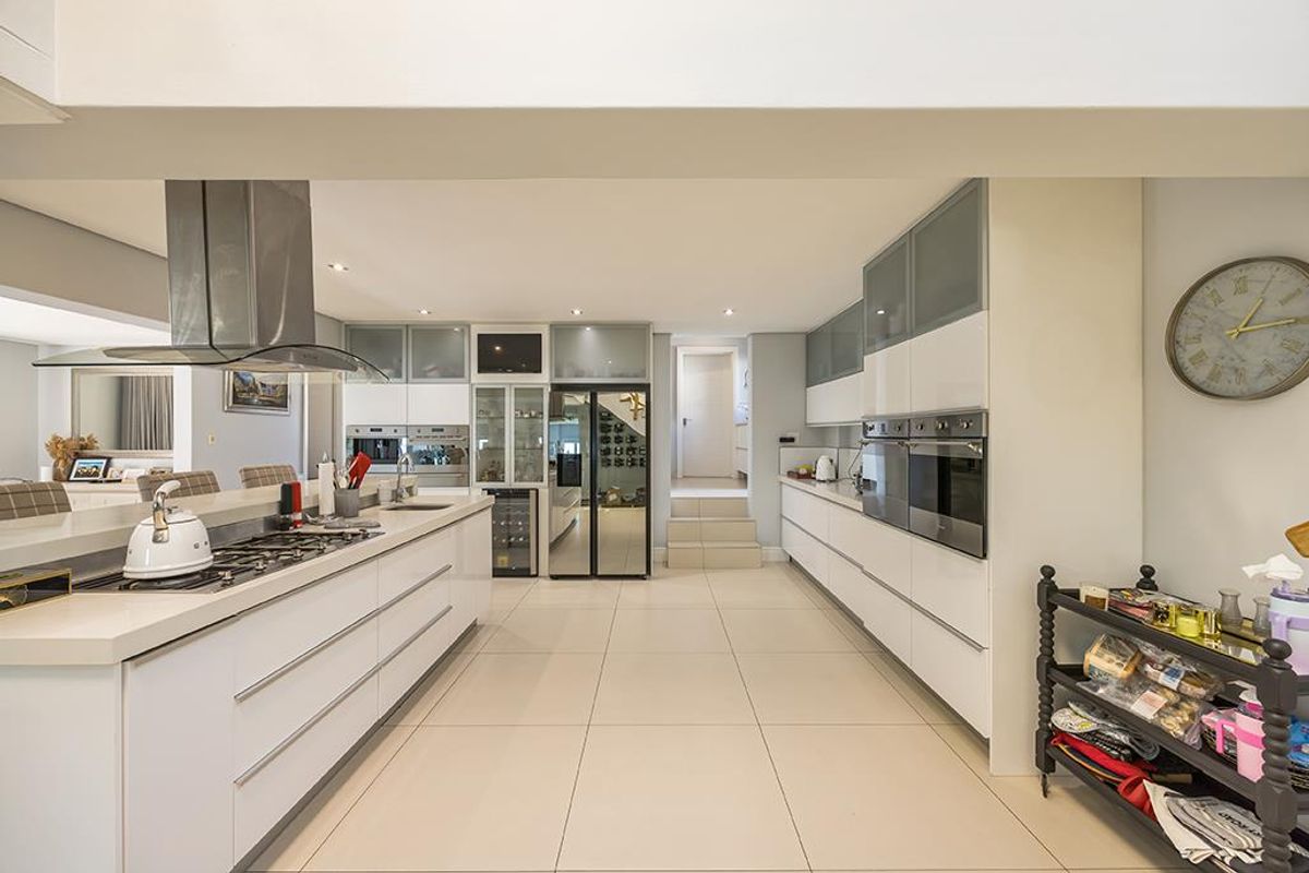 Modern open-plan kitchen featuring sleek white cabinetry, integrated stainless steel appliances, a gas hob with extractor hood, and large format floor tiles.