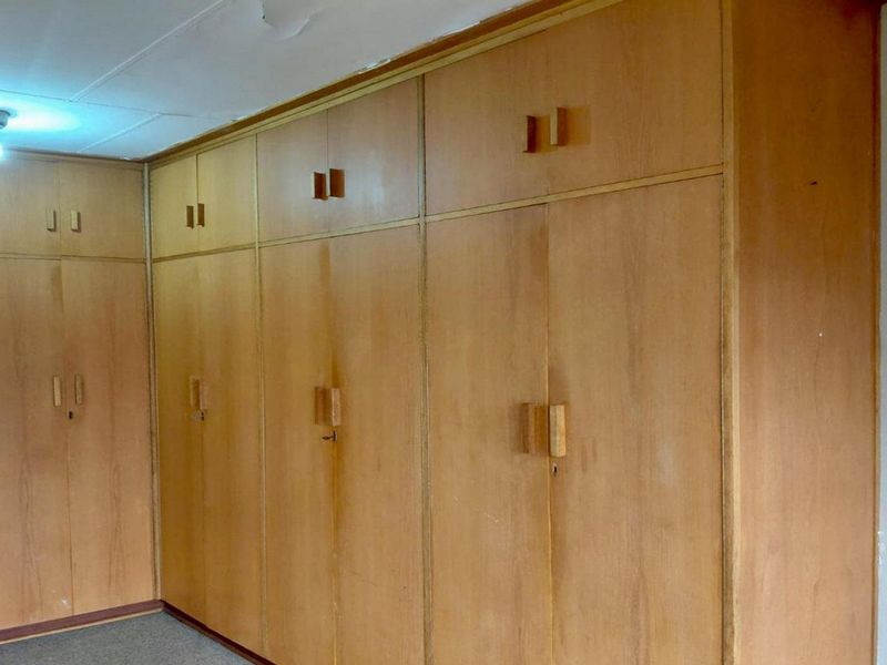 A bedroom featuring extensive floor-to-ceiling built-in wooden cupboards, providing ample storage space. The room is vacant and ready for updates.