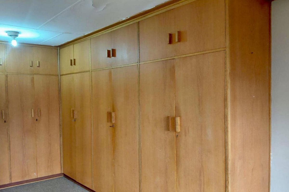 A bedroom featuring extensive floor-to-ceiling built-in wooden cupboards, providing ample storage space. The room is vacant and ready for updates.