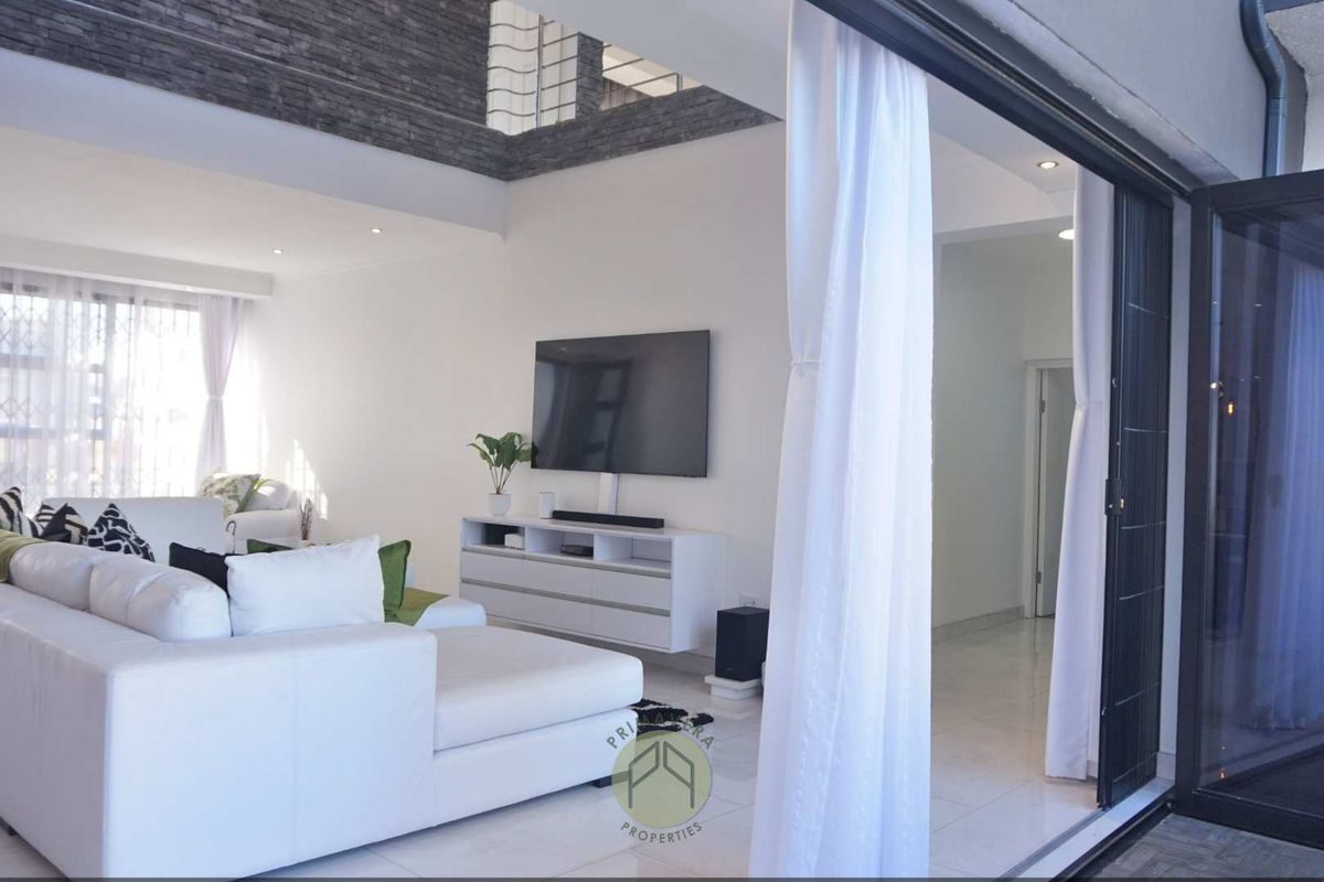 Spacious living area featuring high ceilings with stone-cladding detail, tiled flooring, and large sliding doors opening to an outdoor space.