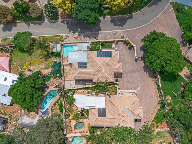 Aerial view of the property showcasing the main dwelling, multiple swimming pools, solar panel installations, tiled roofing, and extensive landscaped garden areas.