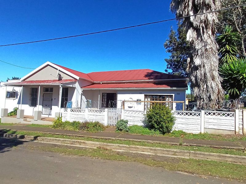Front exterior view of a single-story house featuring a red corrugated metal roof, security fencing, and a gated entrance from the street.