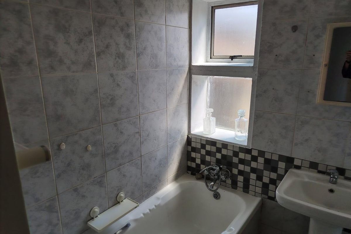 A dated bathroom featuring a standard bathtub, pedestal basin, and tiled walls with a small window for natural light.