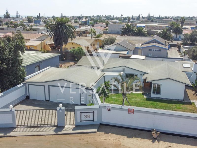 Aerial view of a residential property featuring a house with a tiled roof, double garage, paved driveway, and a secure perimeter wall.