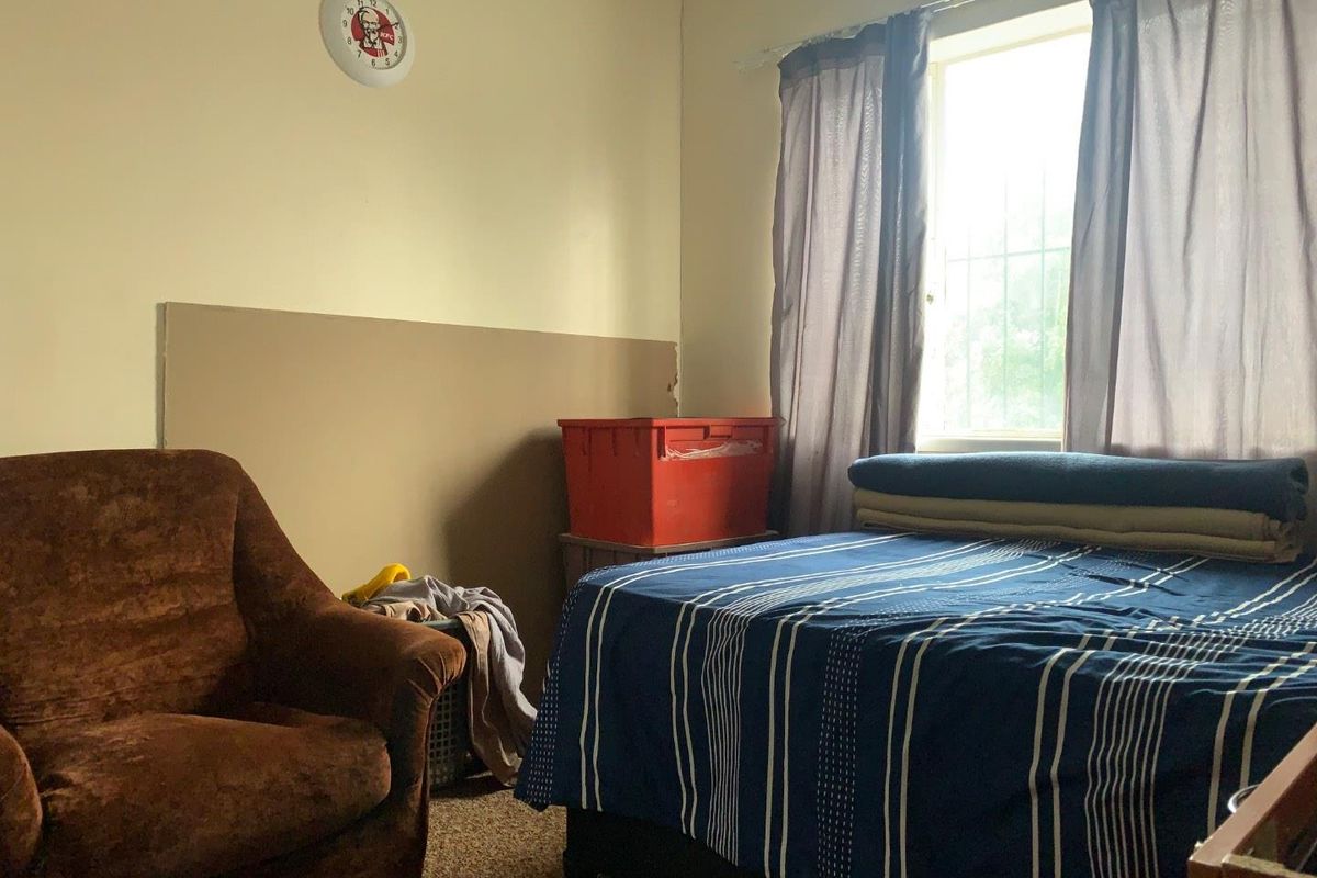 A bedroom featuring a window with security bars and carpeted flooring, providing a functional space for rest.
