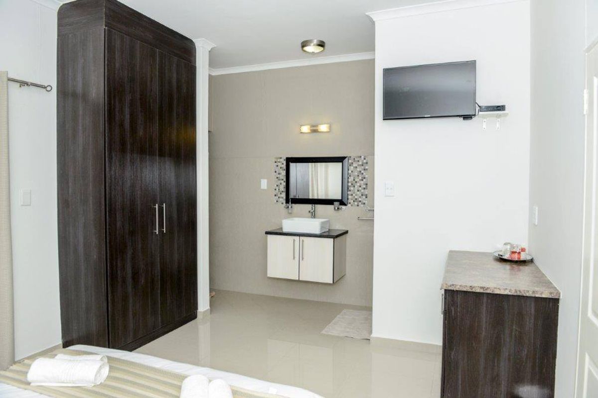 A bedroom featuring a built-in dark wood wardrobe and an integrated vanity area with a modern basin and wall-mounted mirror.