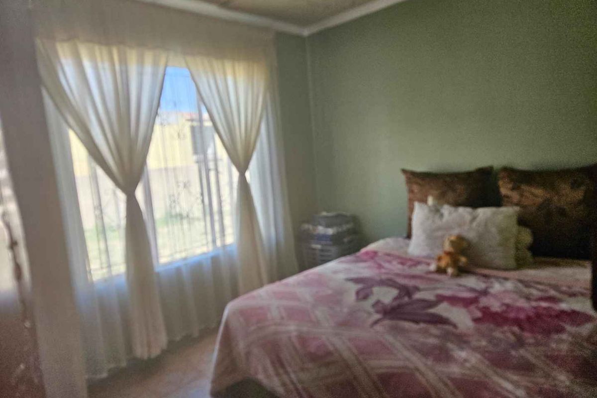 A bedroom featuring a large window with security bars and neutral wall tones, providing a functional space for rest.