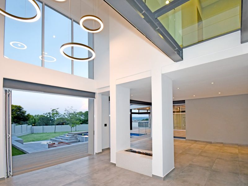 Spacious double-volume living area featuring large format floor tiles, a built-in fireplace, and expansive stacking glass doors opening to the garden and pool area.