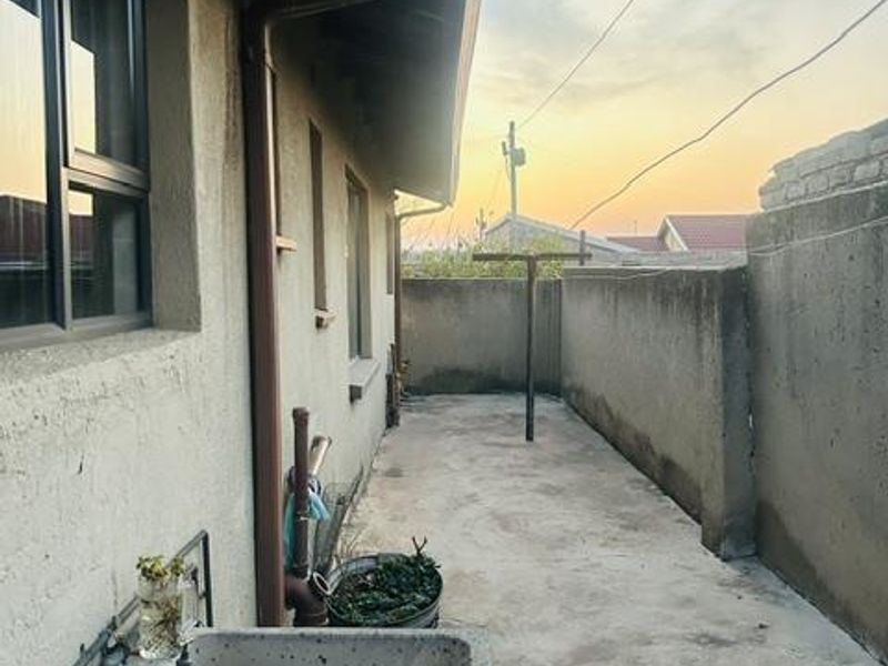 Rear exterior area featuring a concrete wash trough, paved ground, and boundary wall, providing a functional utility space.