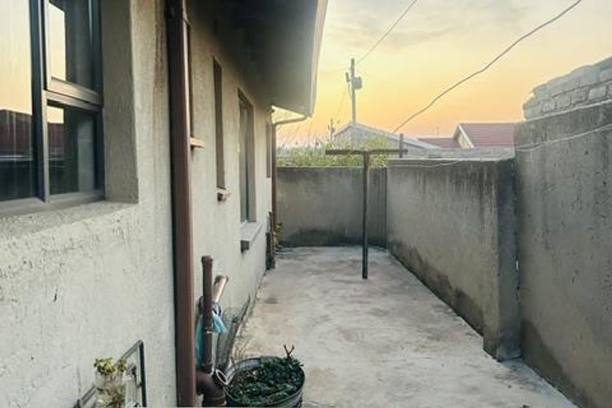 Rear exterior area featuring a concrete wash trough, paved ground, and boundary wall, providing a functional utility space.