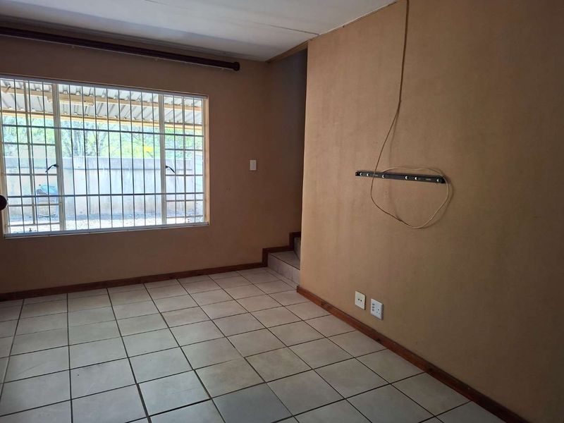 An empty living room featuring tiled flooring, security bars on the window, and a wall-mounted bracket, ready for a fresh update.