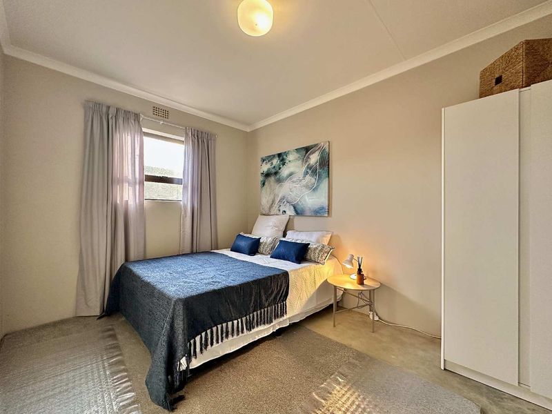 A well-lit bedroom featuring neutral wall tones, a built-in wardrobe, and a window with curtain treatments.