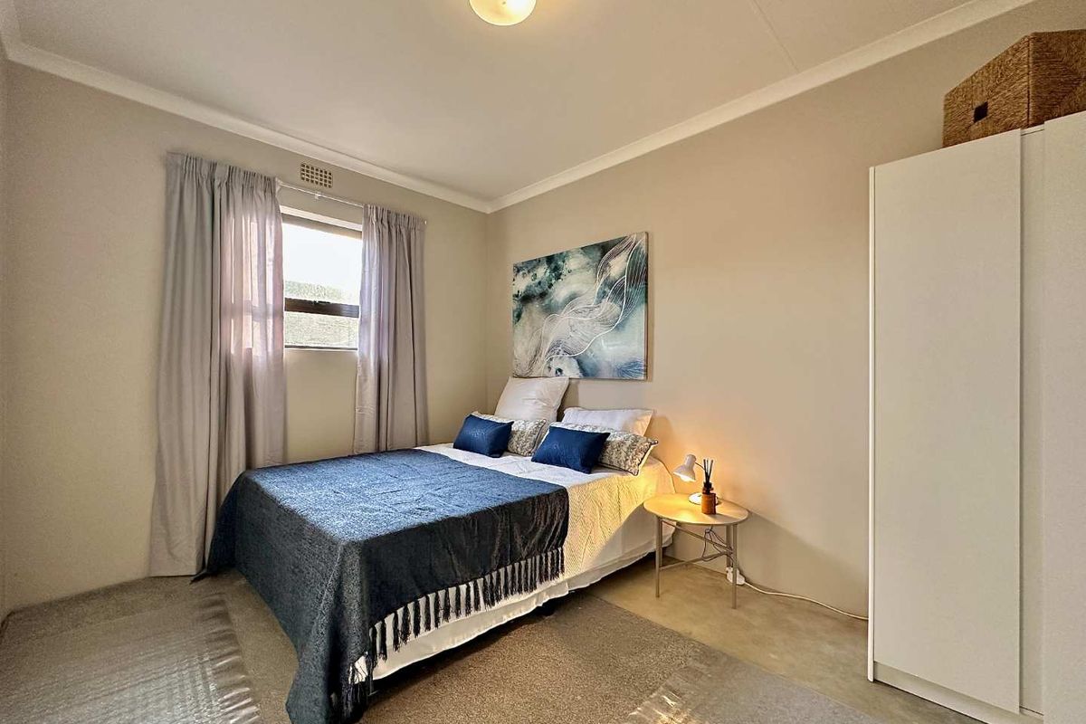 A well-lit bedroom featuring neutral wall tones, a built-in wardrobe, and a window with curtain treatments.
