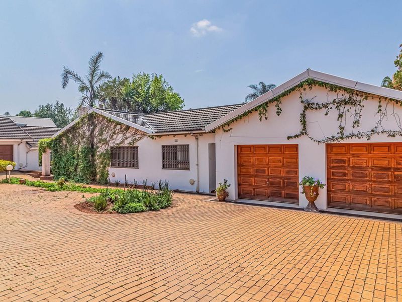 Front exterior view of a single-story house featuring a large brick-paved driveway, multiple garage doors, and a tiled roof.