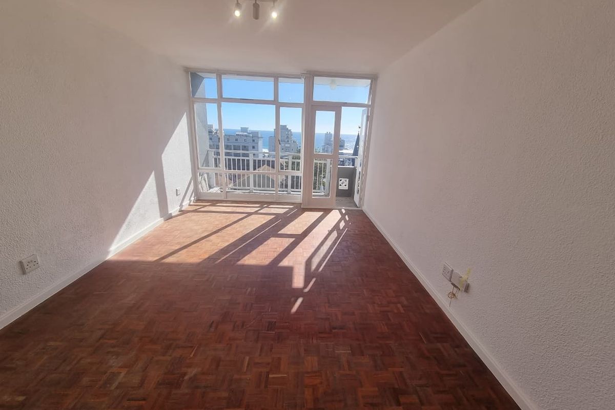 An empty living room featuring original parquet flooring, large windows, and direct access to a balcony with urban and sea views.