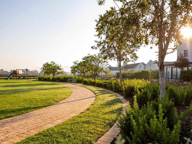 A beautifully landscaped residential garden featuring a curved paved walkway, manicured lawn, mature trees, and established hedging within a well-maintained estate setting.