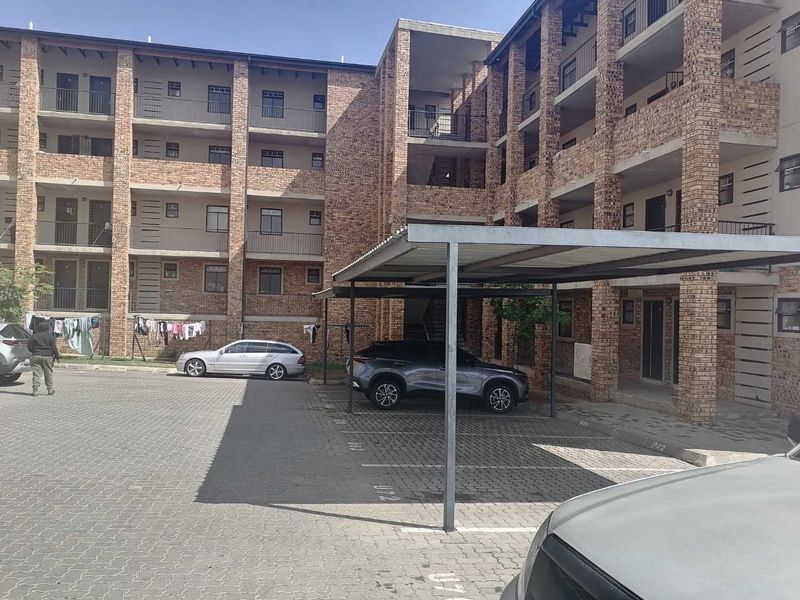 Exterior view of a multi-story face brick townhouse complex featuring paved parking areas and covered carports.