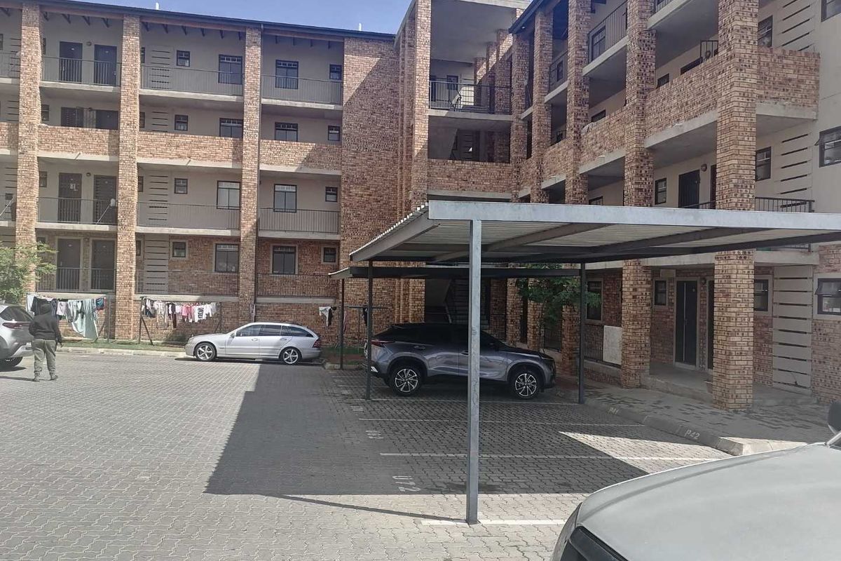 Exterior view of a multi-story face brick townhouse complex featuring paved parking areas and covered carports.
