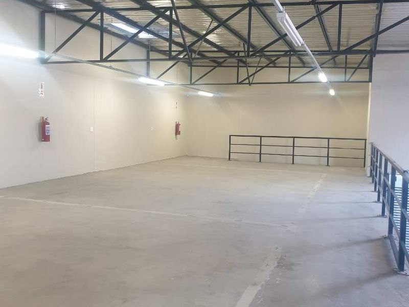 Spacious industrial utility area featuring exposed steel roof trusses, concrete flooring, and integrated safety railings, suitable for storage or workshop use.