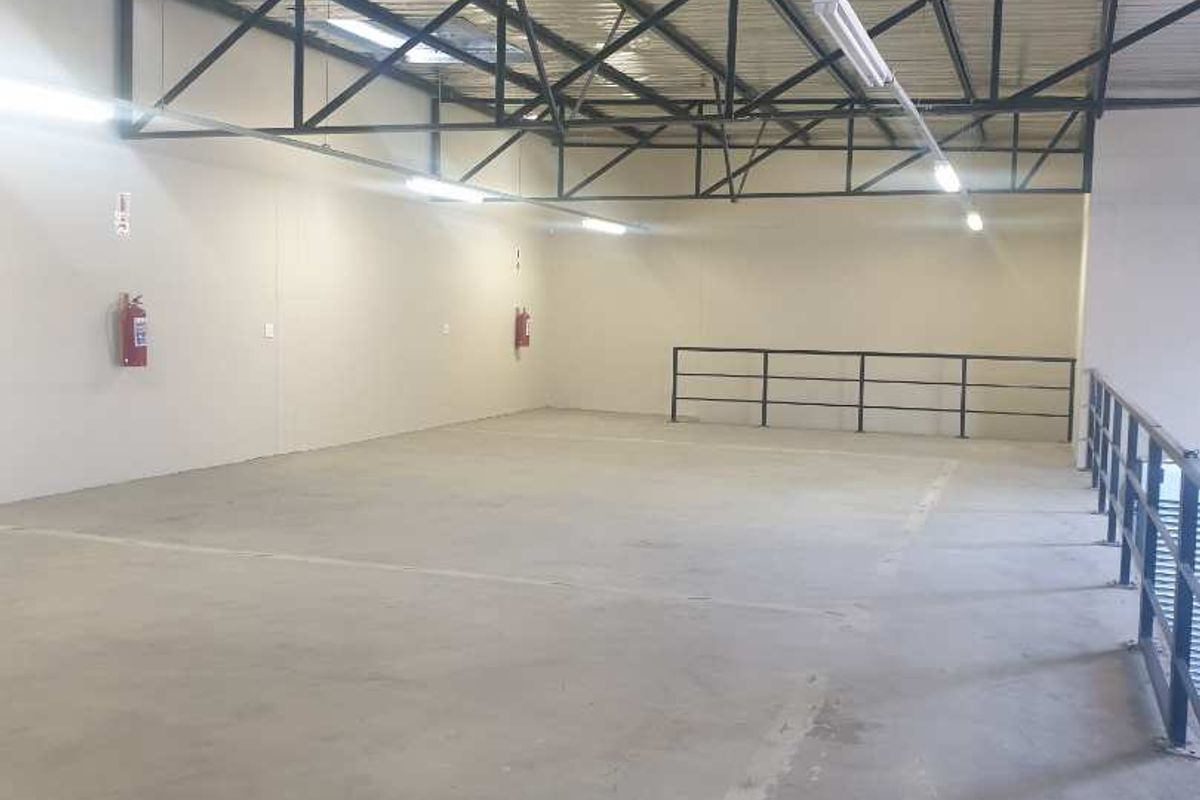 Spacious industrial utility area featuring exposed steel roof trusses, concrete flooring, and integrated safety railings, suitable for storage or workshop use.