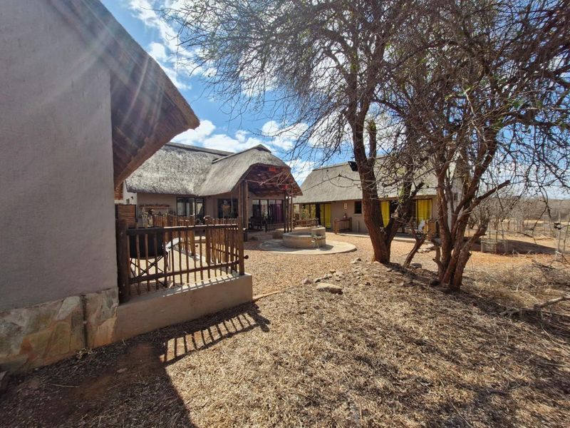 A rear view of the property featuring multiple structures with traditional thatch roofs, a wooden deck, and a central concrete water feature in the garden.