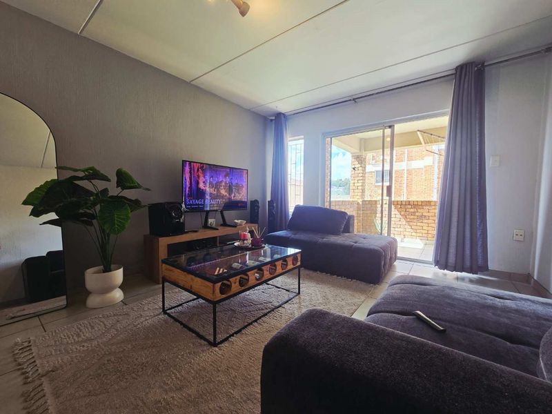 A comfortable living room featuring tiled flooring and a large sliding glass door that provides access to an outdoor balcony area.