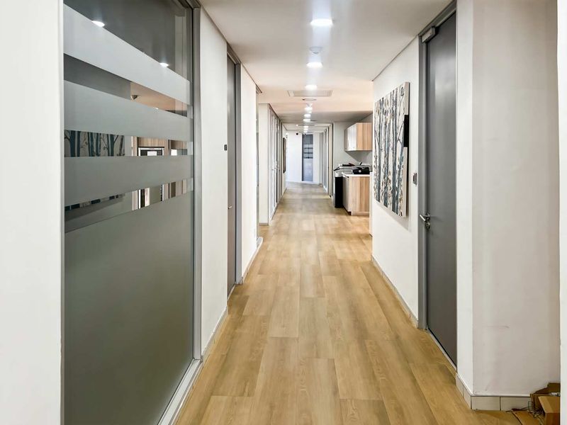 A clean, modern office hallway featuring wood-look flooring, recessed lighting, and professional glass-partitioned office entrances.