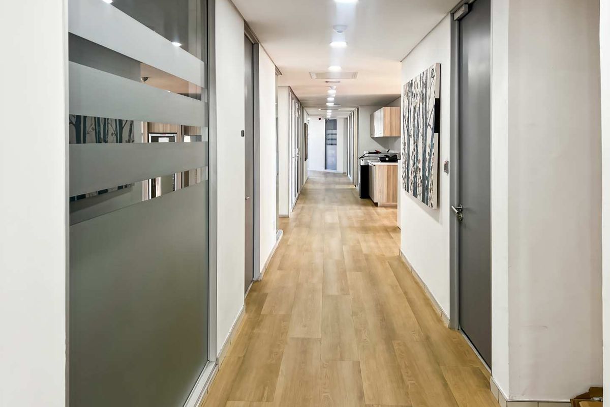 A clean, modern office hallway featuring wood-look flooring, recessed lighting, and professional glass-partitioned office entrances.