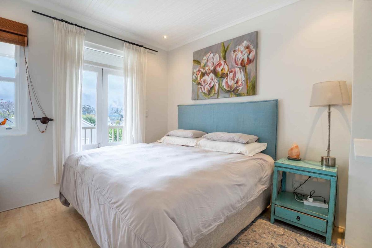 A bright and well-maintained bedroom featuring light timber-look flooring, a tongue and groove ceiling, and direct access to a balcony through french doors.