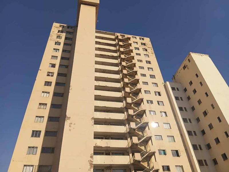 Exterior view of a multi-story apartment building featuring an external fire escape staircase and showing significant signs of exterior paint and render deterioration.