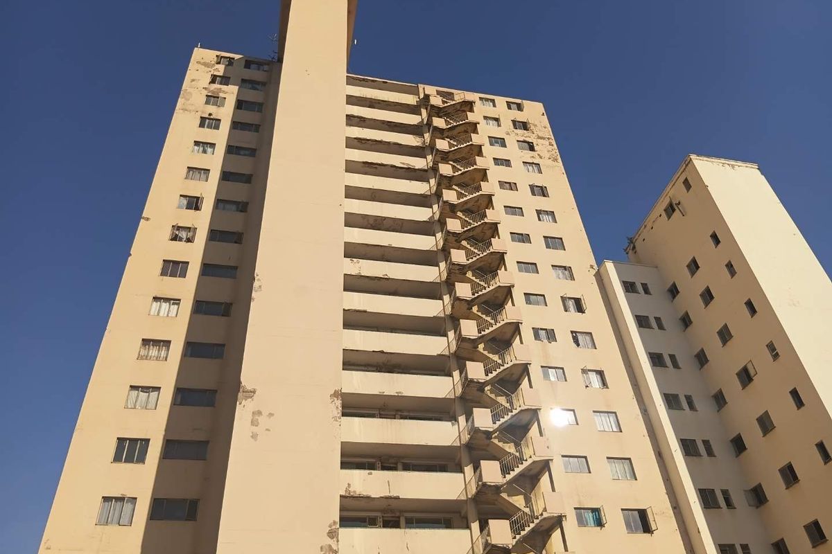 Exterior view of a multi-story apartment building featuring an external fire escape staircase and showing significant signs of exterior paint and render deterioration.