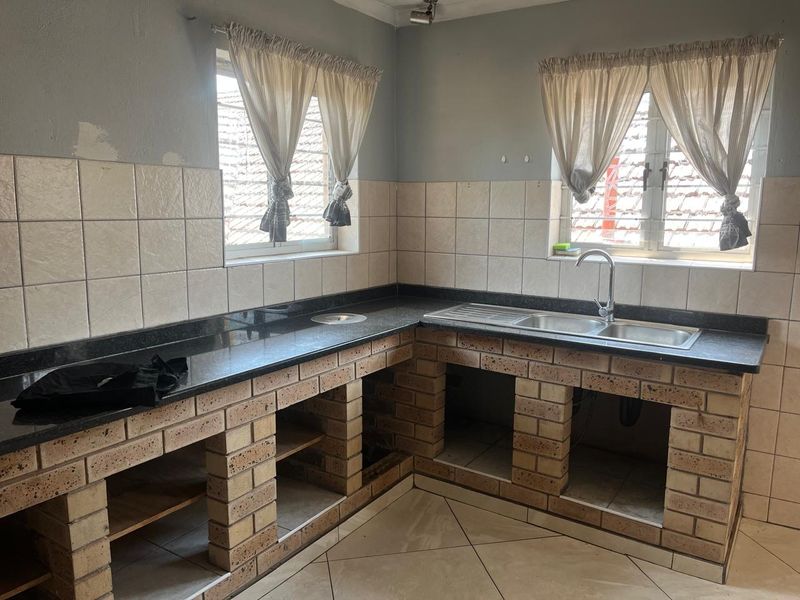 A functional kitchen featuring brick-built cabinetry, granite countertops, and a double stainless steel sink, currently awaiting final finishes and cabinet door installation.