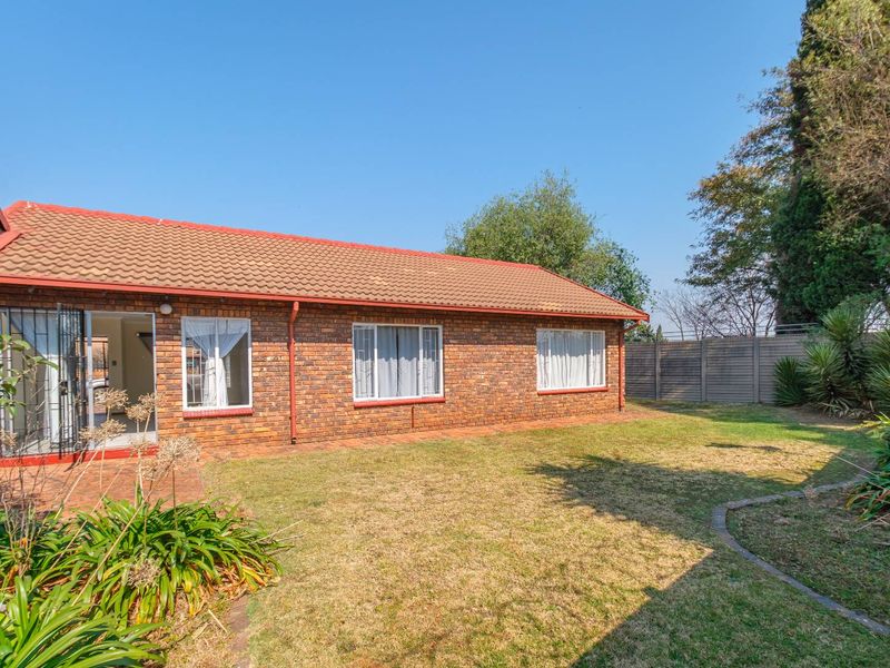 Rear view of the townhouse featuring a face brick facade, tiled roof, paved patio area, and a private garden with perimeter fencing.