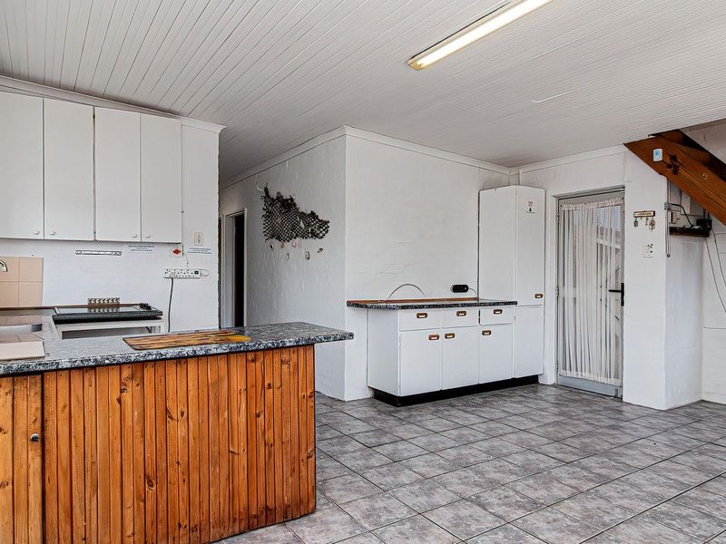 A functional kitchen area featuring built-in cabinetry, laminate countertops, and tiled flooring, with an adjacent timber staircase leading to an upper level.