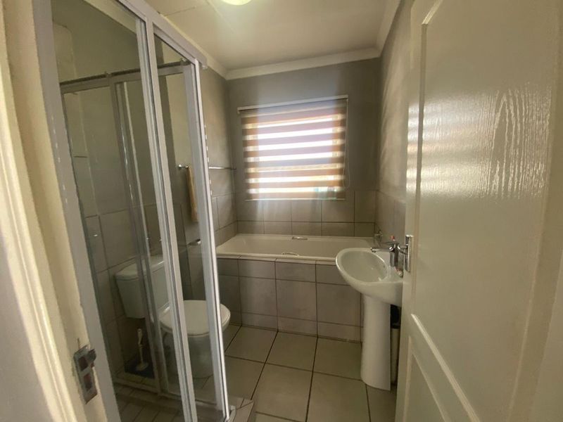 A functional bathroom featuring a shower enclosure, pedestal basin, bathtub, and toilet with neutral tiled finishes.