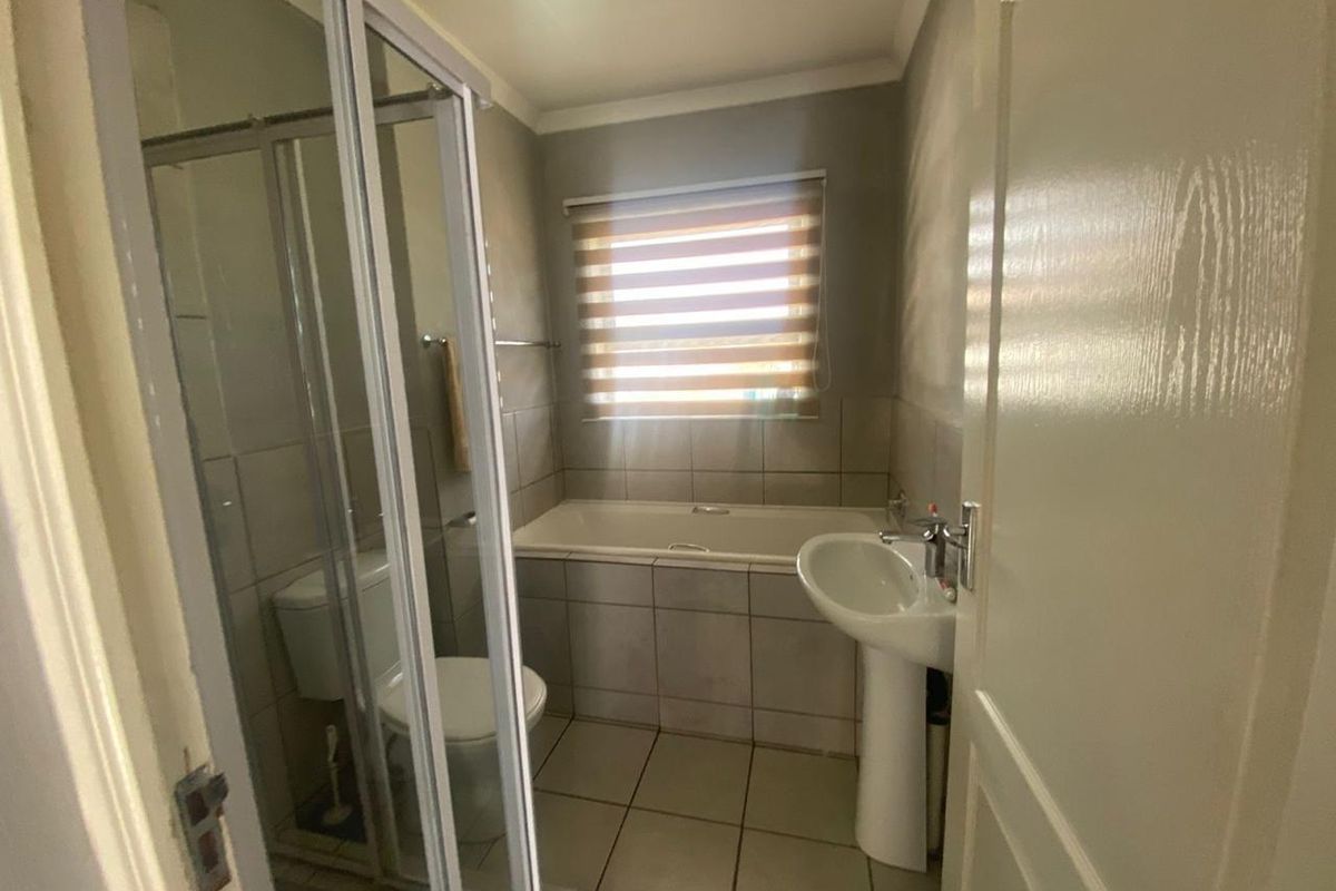 A functional bathroom featuring a shower enclosure, pedestal basin, bathtub, and toilet with neutral tiled finishes.