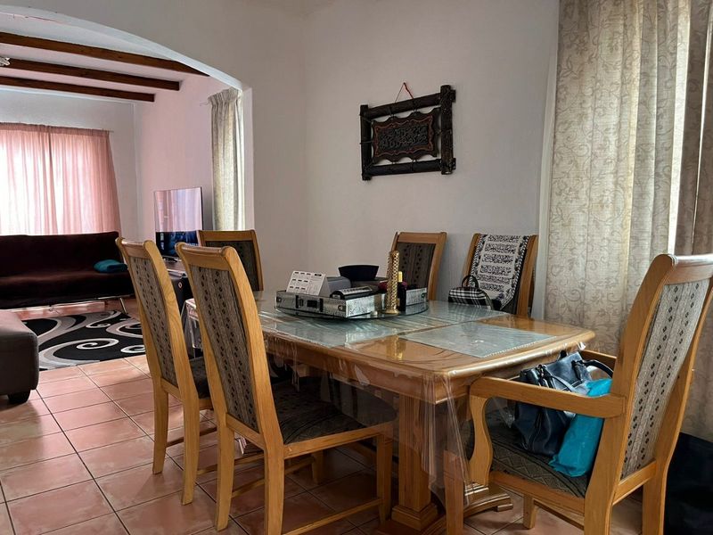 Open plan dining and living area featuring ceramic floor tiles, exposed timber ceiling beams, and an arched transition between the two living spaces.