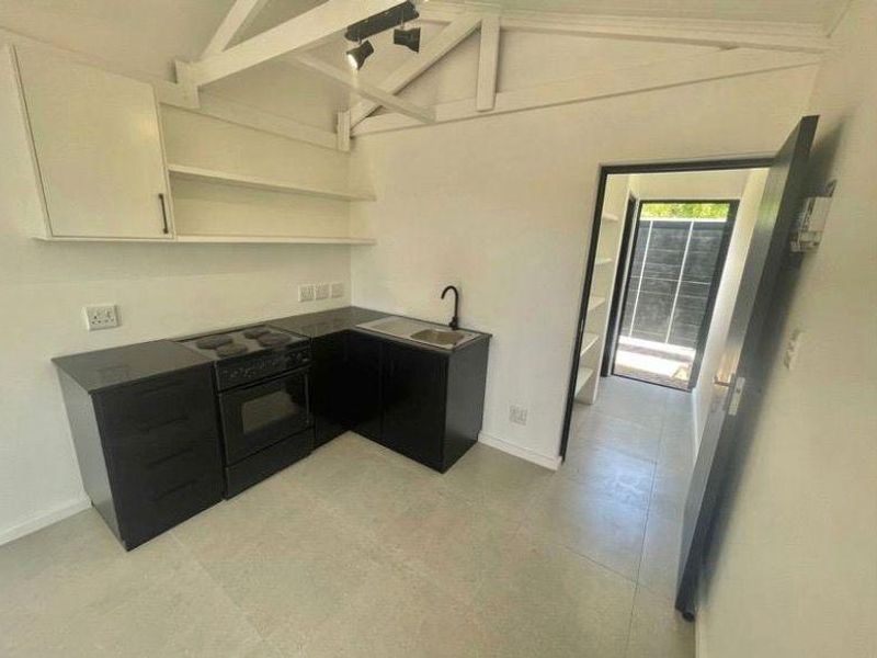 A clean, modern kitchen featuring black cabinetry, an electric stove, oven, and sink, complemented by exposed roof trusses and neutral tiled flooring.