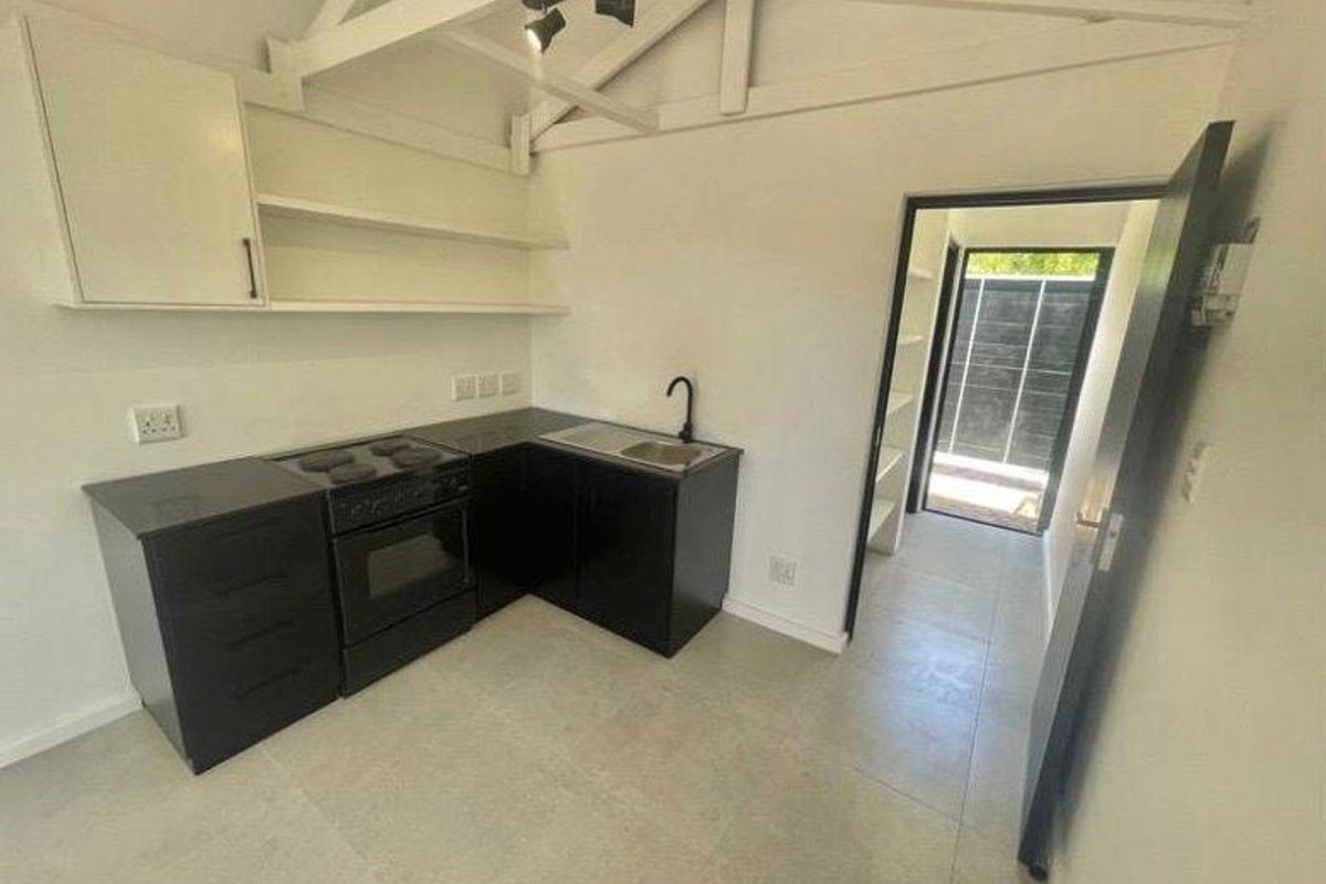 A clean, modern kitchen featuring black cabinetry, an electric stove, oven, and sink, complemented by exposed roof trusses and neutral tiled flooring.