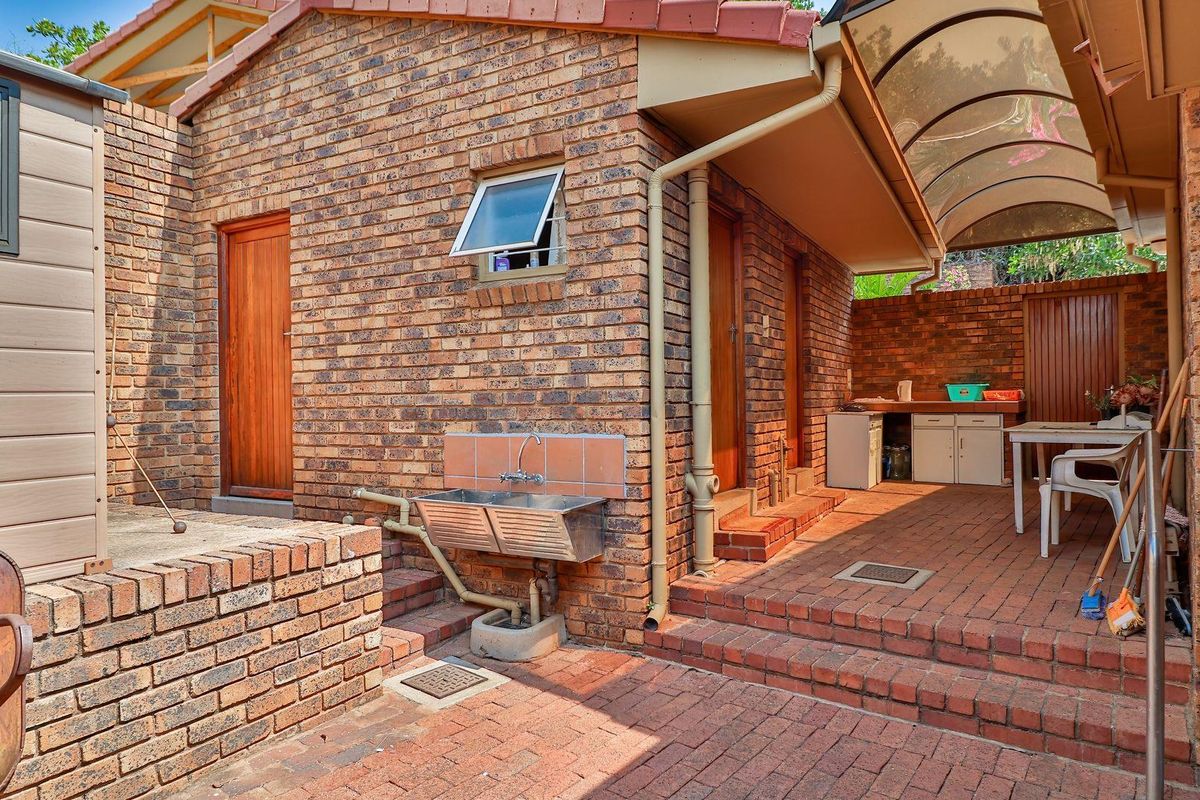 A functional rear courtyard area featuring face-brick construction, a double stainless steel utility sink, and a covered patio section with paved flooring.