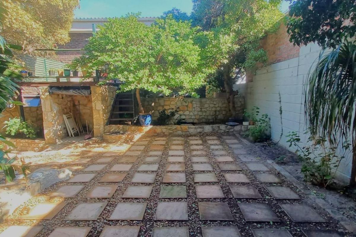 A private rear courtyard featuring stone-paved flooring, a retaining wall, and mature trees, offering a secluded outdoor space.