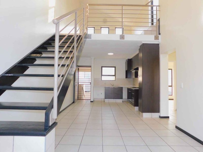 Open-plan living area featuring a modern staircase, mezzanine level, and a functional kitchen with built-in cabinetry and appliances.