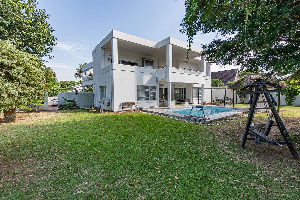 Rear view of a multi-story residence featuring a swimming pool, covered patio areas, and a spacious garden.