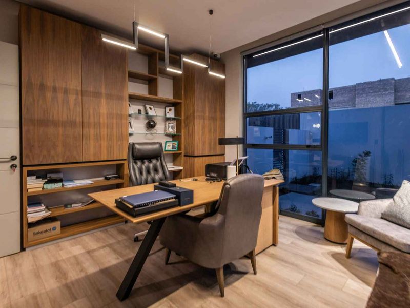 Modern home office featuring custom built-in wooden cabinetry, floor-to-ceiling windows providing natural light, and high-quality laminate flooring.