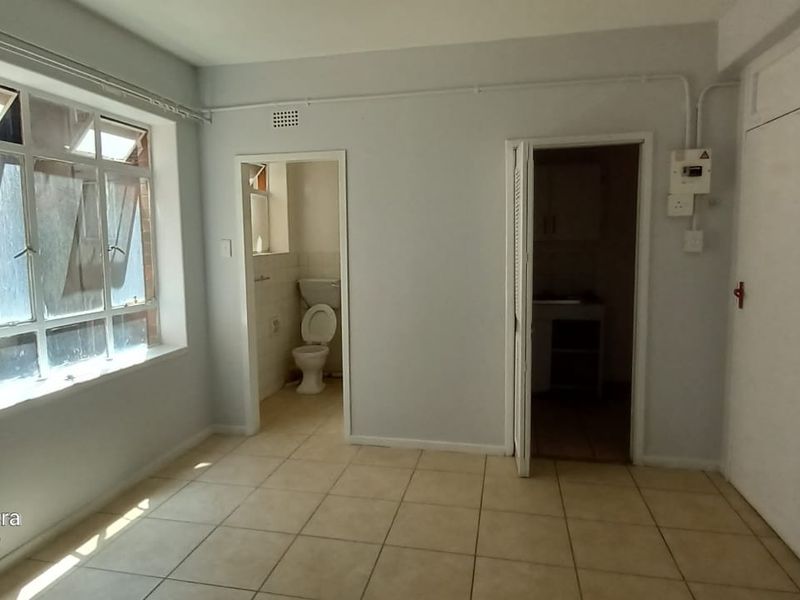 An empty living area featuring tiled flooring, large windows, and direct access to the bathroom and kitchen areas.