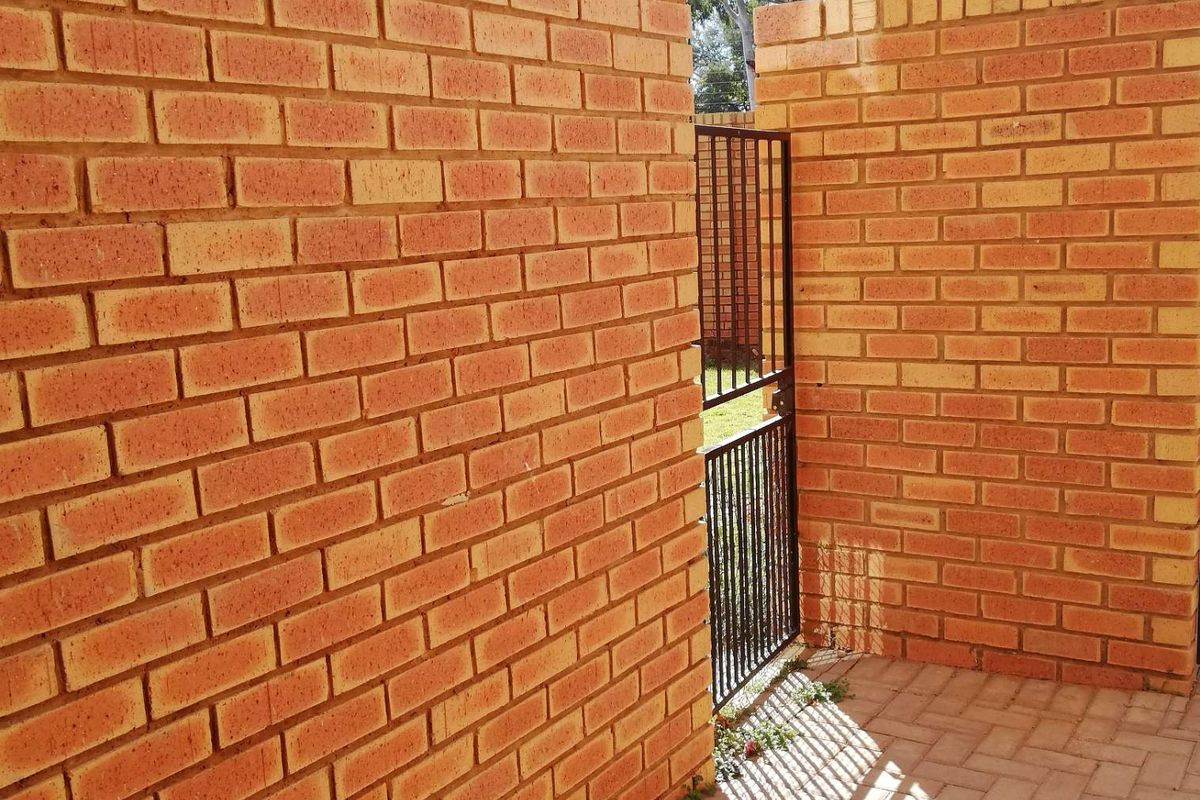 A private rear courtyard area featuring exposed brick walls, paved flooring, and a secure metal gate providing access to the exterior.
