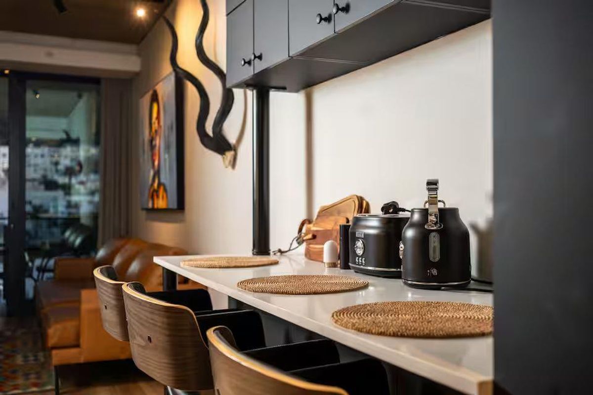 A modern kitchen breakfast bar area featuring sleek dark cabinetry, a clean countertop, and integrated lighting, seamlessly connecting to the living space.