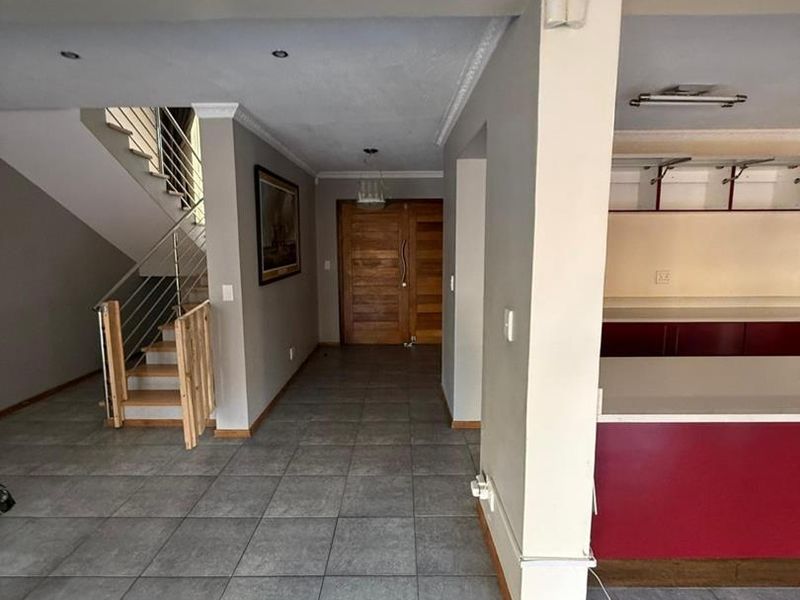 Open plan living area featuring tiled floors, a staircase with stainless steel balustrades, and a partial view of the kitchen cabinetry and entrance.