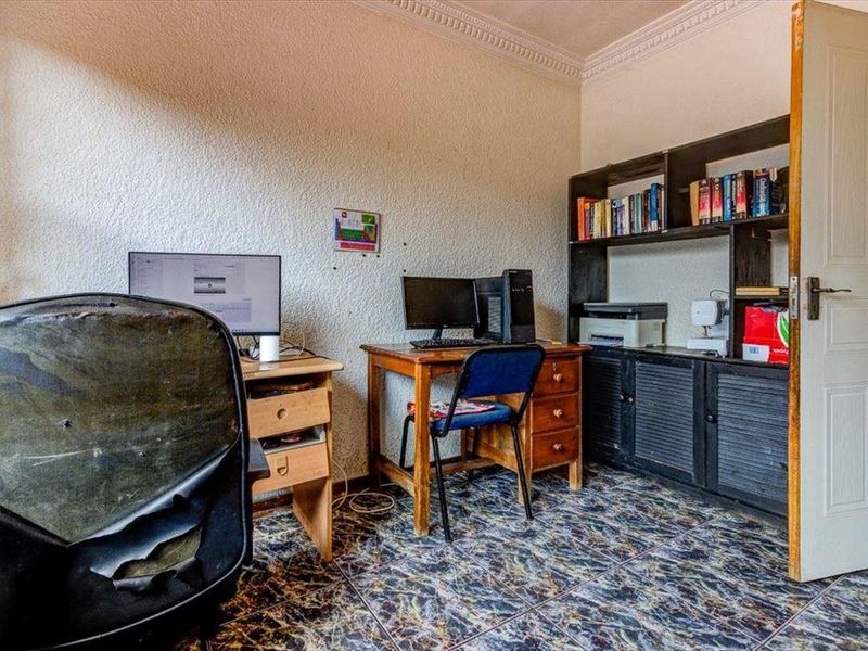 A functional home office space featuring tiled flooring, built-in shelving, and decorative ceiling coving.