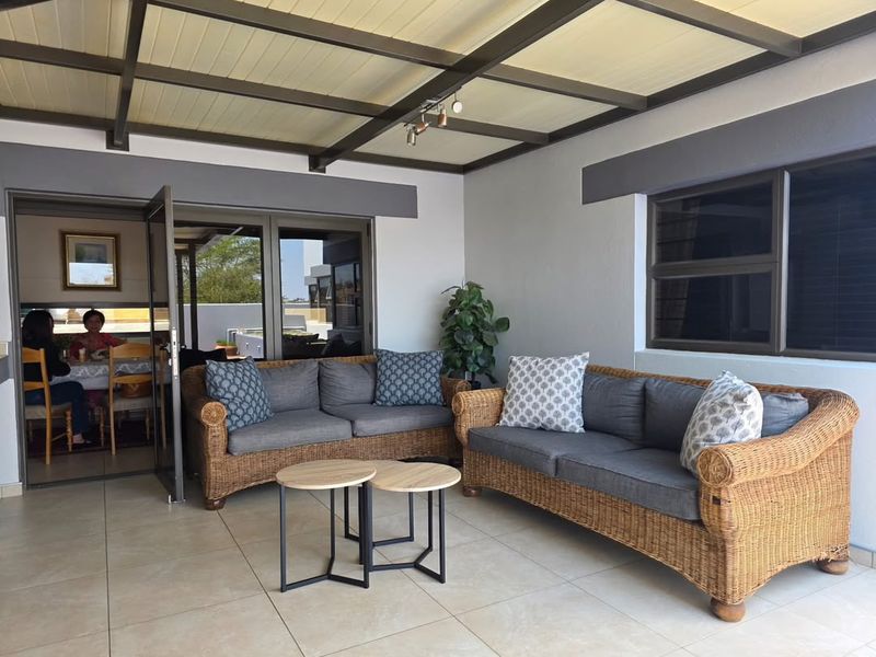 A spacious covered patio featuring tiled flooring, exposed beam ceiling, and large aluminium-framed doors providing seamless access to the interior living area.